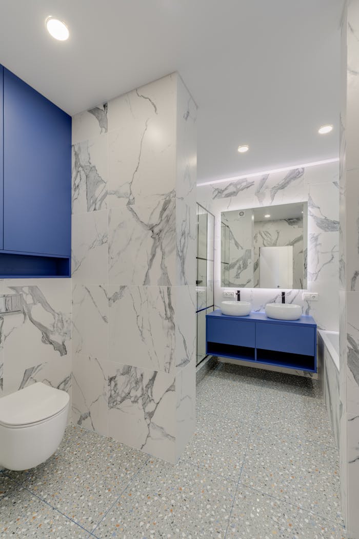 Elegant bathroom featuring blue cabinetry, marble walls, and twin sinks for a luxurious feel.